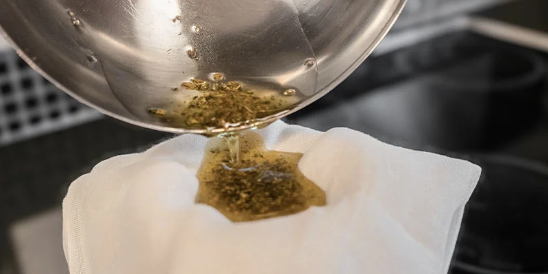 Verwende ein Seihtuch oder ein feines Sieb, um das gesamte Pflanzenmaterial zu entfernen, da das THC nun extrahiert wurde. 